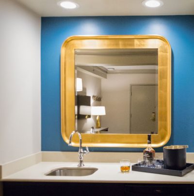 Rounded-corner square bathroom mirror in a blue wall.