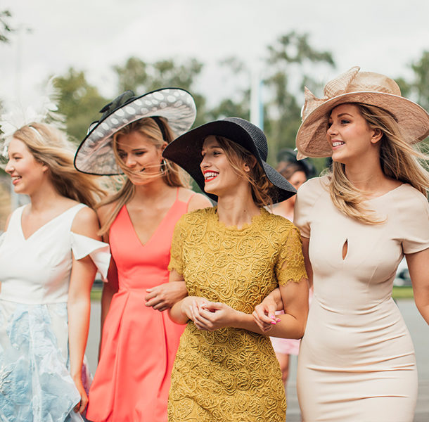 four women in kentucky derby fashions walking and smiling